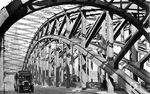 Blick in die Kölner Hohenzollernbrücke über den Rhein in ihrer Entstehungsbauausführung (1911 - 1945) mit drei nebeneinander liegenden Brückenteilen mit jeweils drei Eisenfachwerkbögen (Durchfahrtöffnungen) in Längsrichtung mit vier Eisenbahngleisen und einer Straße. Über die Brücke rumpelt gerade eine preußische P 8 vom Hauptbahnhof nach Köln-Deutz, auf der Straße ist der Bus nach Lindlar unterwegs. (1932) <i>Foto: DLA Darmstadt (Bellingrodt)</i>