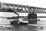 Die Rheinbrücke bei Wesel wurde in den Jahren 1872 bis 1874 von der Cöln-Mindener Eisenbahn-Gesellschaft als Teil der Hamburg-Venloer Bahn über Münster (Westf)—Haltern (Westf)—Wesel—Geldern erbaut und war die nördlichste Rheinbrücke Deutschlands. Die Brücke wurde am 10. März 1945 von der deutschen Wehrmacht gesprengt und nicht wieder aufgebaut. Ein militärische Hilfsbrücke war zwischen 09.04.1945 und Frühjahr 1946 in Betrieb und dann mit endgültiger Streckenschließung wieder demontiert. Über die Brücke fährt gerade eine Geldener 64 mit einem Personenzug von Wesel über Büderich in die Heimat zurück.  (1934) <i>Foto: RVM</i>