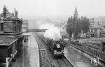 An einem regnerischen Sommertag fährt SNCF 231 K 27 mit dem "Flèche d’Or" nach Paris durch den Bahnhof Boulogne-Tintelleries. Der Luxuszug aus London, der auf britischer Seite "Golden Arrow" hieß, wurde bis 1969 zwischen Calais und Amiens noch mit Dampflok gefahren. Dabei kamen Pacific-Loks der Reihe 231 K zum Einsatz. Der "Flèche d’Or" war damit in Westeuropa der letzte reine 1.-Klasse-Zug, der planmäßig von einer Dampflokomotive gezogen wurde. Die 231 K konnte bis zu 3000 PS leisten und 600 t schwere Schnellzüge mit 120 km/h befördern. Der Blick von der Straßenbrücke der Rue Dutertre in Boulogne hat sich bis heute kaum verändert, lediglich die Fußgängerüberführung im Bahnhof musste der Elektrifizierung weichen. (05.1969) <i>Foto: Robin Fell</i>