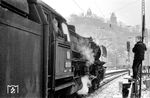 Wie weckt man den Eisenbahnbazillus? 03 1055 zeigt sich in ihrem letzten Einsatzwinter 1964/65 auf der Ruhr-Sieg-Strecke in Altena. Die E-Masten stehen schon. Der Junge ist auf den nicht gerade stabilen Holzzaun geklettert und hält sich am Verkehrsschild des Parkplatzes fest. So kann er den Lokführer der 03 1055 besser beobachten, ja geradezu fixieren bei seinen Handlungen zum Start des großen Dreizylinder-Renners in Richtung Siegen. Die Lok zeigt sich im berühmten Schmuddel-Look einer Maschine, die im Dauereinsatz fährt. Doch Ehrensache der Hagen-Eckeseyer Lokführer war es, egal wie dreckig die Maschine war, die Beschilderung wurde immer gewienert. Die Ausfahrt ist frei, der Heizer hat auf seiner Seite schon den Auftrag des Zugführers entgegengenommen und los geht's. Die unverkennbare Dreizylindermelodie wird in dem engen Tal anschließend eindrucksvoll erklingen, während wegen des naßkalten Wintertages die Dampffahne noch lange den Blick auf die Burg Altena vernebeln wird - eine Erinnerung, die lange nachwirken wird. (03.1964) <i>Foto: Hermann Gerdes</i>