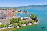 Blick auf Lindau mit dem ehemaligen Hauptbahnhof, Hafen, Bodensee und 18 478 im alten Bw-Bereich. Da die Vorstandsetage der DB AG allem Anschein nach eine weitreichende Aversion gegen Kopfbahnhöfe besitzt, sollte im Rahmen des Projekts "Bahnhof 21" der Kopfbahnhof auf der Insel komplett aufgegeben und durch den Durchgangsbahnhof Lindau-Reutin auf dem Festland ersetzt werden. Das Vorhaben scheiterte (zum Glück) am Widerstand der Stadt sowie am Ergebnis zweier Bürgerentscheide, welche allesamt den – zumindest teilweisen – Erhalt des Insel-Bahnhofs forderten. So wurden die Pläne in der geänderten Form einer Kombilösung aus dem Bahnhof Lindau-Reutin und dem Weiterbetrieb des Insel-Bahnhofs in reduziertem Umfang umgesetzt. Die erhoffte Beschleunigung des Fernverkehrs und Steigerung der Fahrgastzahlen mit der parallelen Aufgabe der Fernzüge über die Allgäustrecke blieb allerdings aus, da die Bahn weiterhin nicht in der Lage ist, ihre Fernzüge halbwegs pünktlich über ihr Netz zu fahren. Dafür wurde der Vorteil geopfert, Fahrgäste umsteigefrei direkt bis zum Bodenseeanleger zu befördern. Das Ergebnis dieser Entscheidung zeigt sich nun im alltäglichen Wochenend-Verkehrschaos auf der Insel. (01.05.2025) <i>Foto: Joachim Schmidt</i>
