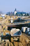 Bau des Siegauen-Tunnel der Schnellfahrstrecke Köln–Rhein/Main. Der Tunnel galt als der schwierigste Bauabschnitt der ganzen Neubaustrecke. Er unterquert auf 2.502 m die Siegaue, die Sieg, die A 560, einen Teil von Niederpleis mit dem Gemeindezentrum Sankt Martinus (Foto), einen Friedhof und die Pleisbachaue zwischen Siegburg und Sankt Augustin. Der Tunnel war in der ursprünglichen Planung nicht vorgesehen und geht auf örtliche Forderungen zurück. Anfänglich sollte an seiner Stelle nur eine oberirdische Trasse mit zwei Brücken gebaut werden. Auf einer Länge von 2132 m wurde der Tunnel dann ab Juli 1999 in offener Bauweise errichtet. Insgesamt wurden rund 175.000 m³ Beton, etwa 19.000 t Bewehrungsstahl, rund 16.000 m² Spundwände, zirka 30.000 m² Rammträgerverbau und etwa 26.000 m² Pfahlwände verbaut. Die Sieg wurde auf einer Länge von 150 m verlegt. Für einen Bahndamm wurden rund 150.000 m³ Boden verwendet. Insgesamt wurden 750.000 m³ Baugrund ausgehoben. Ein Teil des Tunnelaushubs wurde entlang der A 3 aufgeschüttet und anschließend begrünt. (03.2000) <i>Foto: Udo Kampschulte</i>