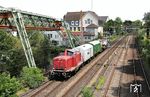 V 100 2299 der Vulkan-Eifel-Bahn Betriebsgesellschaft Gerolstein transportiert zwei Werkstatt- und einen Trafowagen im DGS 69449 (Dortmund-Zinkhütte - Rheydt-Geneicken) vor dem Gerüst der Schwebebahn in Wuppertal-Barmen. (10.07.2025) <i>Foto: Uwe Meiß</i>