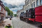 Erhöhte Aufmerksamkeit erfordert die Fahrt der 99 2322 durch die Mollistraße in Bad Doberan. Das Lokpersonal muss jederzeit mit unbedachten Autofahrern oder Passanten rechnen. Zur Entstehungsgeschichte des Namens "Molli" gibt es viele unterschiedliche Geschichten. Am weit verbreitesten ist die Anekdote über einen kleinen dicken Mops namens "Molli": Vor mehr als einhundert Jahren reiste eine alte Dame mit ihrem kleinen Hund nach Bad Doberan. Natürlich wollte auch sie mit der neu eröffneten Dampfeisenbahn von Bad Doberan nach Heiligendamm fahren. Doch ihr Mops war unter keinen Umständen zum Einsteigen zu bewegen. Als der Hund ausriss, rief die alte Dame ihm noch hinterher: "Molli, bliev stahn!" (plattdeutsch für "Molli, bleib stehen!"). Doch nicht etwa der Mops hörte auf diesen Ruf, sondern der Lokführer brachte seinen gerade angefahrenen Zug zum Halten. Fortan hieß die kleine Bäderbahn im Volksmund "Molli". (25.06.2025) <i>Foto: Joachim Schmidt</i>