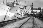 Eine interessante Ansicht aus dem Hamburger Hafen, die zeigt, dass selbst Ozeandampfer von dem Gewicht der Lokomotiven ins Schwanken gerieten. Da die Kaikräne am Schuppen 59 zu schwach sind, wird die Krupp-Lok für Tsingtau in China über das bordeigene Ladegschirr an Bord der "Belmora" gehieft. (24.10.1936) <i>Foto: Gustav Werbeck</i>