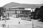 Gegenüber des heutigen Bahnhof Neustadt (Weinstr) Hauptbahnhof, der bis 1935 sowie von 1945 bis 1950 den Namen Neustadt (Haardt) trug, befindet sich nur durch den Bahnhofsvorplatz getrennt der sog. Saalbau. Der Saalbau wurde als Veranstaltungszentrum in den Jahren 1871 bis 1873, als die Pfalz zum Königreich Bayern gehörte, vom Münchener Architekten Albert Geul im Stil der Neorenaissance errichtet. Ein Großbrand in der Nacht vom 24. auf den 25. November 1980 beschädigte den Saalbau schwer und machte ihn unbenutzbar. Von 1982 bis 1984 wieder er wieder neu aufgebaut. Das Bild zeigt den Saalbau mit Bahnhofsvorplatz Mitte der 1930er Jahre. Die Straßenbahn gehört zur Pfälzer Oberlandbahn, die nach Landau (Pfalz) führte und 1955 stillgelegt wurde. (1934) <i>Foto: RVM</i>
