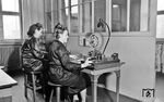 Zwei Bedienstete der Fernschreibstelle in der Wuppertaler Reichsbahndirektion beim Versenden von Telegrammen über die Morse-Telegraphen. An der Wand hängen Schilder für den Anwahlcode in die jeweiligen Bezirksleitungen, die zur Kommunikation zwischen den Dienststellen verwendet wurde. Die Bezirksleitungen ermöglichten eine effiziente Nachrichtenübermittlung zu allen Haupt- und Nebenbahnen, indem sie die Stationen direkt verbanden. (1941) <i>Foto: RBD Wuppertal (Eckler)</i>