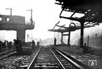 Bereits unmittelbar nach Ende des Luftangriffs begannen die Reparaturarbeiten im Bahnhof Opladen, meist durch Kriegsgefangene. Das Bild zeigt die Einfahrt aus Richtung Leichlingen mit dem zerstörten Stellwerk "Pn" am nördlichen Ende des Bahnsteig II. Das Stellwerk wurde nicht wiederaufgebaut, sondern in einem MDi-Wagenkasten (ex "Dresden 300065") behelfsmäßig wieder in Betrieb genommen (vgl. Bild-Nr. 91292, 91294). Schemenhaft ist das Empfangsgebäude von 1867 zu erkennen, sowie ein in Gleis 2 stehender Dampfzug. Die zerstörte Bahnsteigüberdachung (rechts) gehört zu den Gleisen 36/37, in denen die Personenzüge in/aus Richtung Immigrath/Hilden begannen und endeten. (28.12.1944) <i>Foto: Karl Wolter</i>