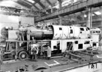 Bei höheren Geschwindigkeiten spielt der Luftwiderstand einer Lokomotive eine entscheidende Rolle. Dieser ergibt sich aus dem Querschnitt der Lokomotive, einem Widerstandsbeiwert und dem Quadrat der Geschwindigkeit. Ein höherer Eigenwiderstand der Lok bedeutet, dass bei gegebener Kesselleistung immer weniger Kraft am Zughaken übrig bleibt. Die Reichsbahn experimentierte daher vor dem Erscheinen der Baureihe 05 mit zwei Loks der Baureihe 03. Neben der teilverkleideten 03 154 erhielt die hier im Bau befindliche 03 193 eine vollständige Stromlinienverkleidung. Die Borsig-Werkaufnahme zeigt das Anbringen der Verkleidung von Kessel und Triebwerk. Der Oberflächenvorwärmer fand dabei keinen Platz mehr vor dem Schornstein der verjüngten Rauchkammer, sondern wurde in der Blechversteifung oberhalb des Pufferträgers angeordnet. (09.1935) <i>Foto: Werkfoto</i>