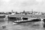Vor der zerstörten Magdeburger Stadtkulisse passiert das Frachtschiff "Aufbau" die behelfsmäßig wiederaufgebaute Strombrücke. Nach 83 Jahren wurde die eiserne Strombrücke im April 1945 durch die Deutsche Wehrmacht gesprengt. Die Amerikaner, die am 11. April 1945 Magdeburg besetzten, errichteten eine Behelfsbrücke, die als „Brücke der Freundschaft“, ab dem 2. Juni 1945 für den Verkehr genutzt werden konnte. Parallel dazu verlief oberhalb der Strombrücke eine von der Roten Armee im Sommer 1945 errichtete Pontonbrücke. Beides waren Provisorien. Am 29. April 1946 wurde dann eine Behelfsbrücke aus alten Brückenelementen unter Nutzung vorhandener Pfeiler- und Widerlagerelemente freigegeben (Foto). Der Brückenbelag bestand aus Eichenholz, und die Konstruktion ließ eine Belastung von 60 Tonnen zu. Am 7. Oktober 1965 wurde die 'Neue Strombrücke' als Stahlkonstruktion eröffnet. (07.1956) <i>Foto: Jürgen Hagemann</i>
