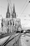 Sie gehören in Köln untrennbar zusammen: Dom und Hauptbahnhof. Neben der "Ewigkeitsbaustelle" des sakralen Bauwerks (die Bauzeit betrug satte 632 Jahre bis ins Jahr 1880 - dagegen ist 'Stuttgart 21' Peanuts) wurde der "Cölner Centralbahnhof" nicht von ungefähr direkt neben dem Dom geplant. Der Standort galt als Breitseite gegen die katholische Kirche, die keine Grundstücke in der Kölner Innenstadt abgeben wollte. Die Lage des Bahnhofs im beengten Platz zwischen Rhein und Dom ist bis heute ein Politikum, da er als zentraler Engpass im Kölner Schienenverkehr gilt. Immer wieder wurde die Verlegung des Hauptbahnhofs gefordert. Übrigens liegt die Hohenzollernbrücke direkt auf die Mittelachse des Domes ausgerichtet, was sicherlich auch kein Zufall war. Am einem Maimorgen des Jahres 1959 zeigen sich in der Ostausfahrt des Hauptbahnhofs 03 1054 (Bw Hagen-Eckesey), 01 233 (Bw Koblenz Mosel) und ein VT 11, der als TEE 168 "Paris-Ruhr" nach Paris in den Bahnhof einfährt.  (05.1959) <i>Foto: Ernst Winter</i>