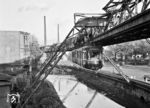 Ein Schwebebahnzug der Baureihe 50 fährt in die Schwebestation 'Adlerbrücke' ein. Die ab 1950 beschfften Wagen sollten die überalterten, zwischen 1900 und 1912 beschafften Fahrzeuge ersetzen. Durch die eine dünnwandige Stahlleichtbauweise konnte das Leergewicht auf 11,0 t vermindert werden, bei gleichzeitiger Kapazitätserhöhung von 65 auf 80 Plätze. Damit war die Baureihe 50 um 1,3 bis 2,9 Tonnen leichter als ihre verschiedenen Vorgängerbaureihen. Die hohen Schornsteine im Hintergrund gehören zum Heizkaftwerk Barmen. Der höhere, 137 Meter hohe Kamin war damals der höchste Ziegelstein-Schornstein Deutschlands. (23.06.1962) <i>Foto: Basil Roberts</i>