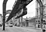 Eine Schwebebahn schwebt kurz vor der Station 'Sonnborner Straße' über die gleichnamige Straße in Wuppertal-Sonnborn und trifft dort auf eine Straßenbahn der Linie 1 nach Zoo/Sonnborn. (23.06.1962) <i>Foto: Basil Roberts</i>