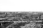 Blick vom Humboldthain auf den Bahnhof Berlin Gesundbrunnen. Vor dem Bahnhof sind auf der Brunnenstraße die damals für Berlin typischen Doppeldecker Busse der BVG unterwegs. Im Hintergrund verläuft die Swinemünder Brücke über die Gleise und die Häuser des Bezirks Pankow und Prenzlauer Berg. Ein Zug der Ringbahn (ET 165) verlässt den Bahnhof in Richtung Schönhauser Allee. (04.1959) <i>Foto: Jürgen Hagemann</i>