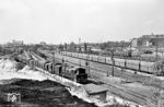 93 230 vom Bw Berlin-Grunewald rangiert im Bahnhof Berlin-Charlottenburg Gbf. Der in Bildmitte abgestellte Kohleleerwagenzug wird zurück ins Ruhrgebiet gehen. Nach dem Helmstedter Abkommen von 1949 erfolgte die Abfuhr der Leerzüge über Stendal – Oebisfelde, für beladene Ganzzüge über Helmstedt – Marienborn. Dahinter steht in der Abstellgruppe des ehemaligen S-Bw Westend ein Dreiviertelzug der Baureihe ET 165 einsatzbereit. Links befindet sich die Baustelle der entstehenden Stadtautobahn A 100. Im Hintergrund sind die Werkstätten und Verwaltungsgebäude der Siemens AG an der Nonnendammallee zu erkennen. (07.1960) <i>Foto: Jürgen Hagemann</i>
