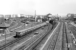 Ein ET 165 der Zuggruppe A "Vollring" fährt vom Bahnhof Schönhauser Allee kommend in den Bahnhof Berlin Gesundbrunnen ein. Links oben im Bild sind noch die Reste des 27-ständigen Ringlokschuppen zu erkennen. Dieser wurde Anfang 1962 wie auch der Wasserturm abgerissen, die Strecke 1961 durch den Mauerbau unterbrochen. Rechts im Vordergrund verläuft das Güterzuggleispaar um das 1952 aufgelassene Bahnbetriebswerk herum in Richtung Bornholmer Straße. In den 1990er Jahren gestaltete man den Bahnhof komplett um und baute ihn zum Fernbahnhof aus. Dabei wurden die gesamten Bahnanlagen konzeptionell umgeplant. (04.1960) <i>Foto: Jürgen Hagemann</i>