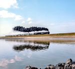 Nach der langen Standzeit der 012er in Westerland (Sylt) war es üblich, bei der Fahrt über den abgeschiedenen Hindenburgdamm die Rohre durch eine in die Feuerbüchse geworfene Schaufel Sand freizublasen. Für die Lok bedeutet dies eine (verbotene) Roßkur, für den Fotografen ein willkommenes Schauspiel, vorausgesetzt man stand genau an der richtigen Stelle. Im August 1972 gelang Ulrich Hesse punktgenau diese Aufnahme der rohreblasenden 012 105 vor dem E 2109 auf dem Hindenburgdamm, während sich die Zuglok 012 077 noch zurückhält. Die Vorspannlok stammte in den Sommermonaten aus dem D 637, die keine Rückleistung nach Hamburg hatte und daher planmäßig Vorspann vor dem Eilzug leistete.  (08.1972) <i>Foto: Ulrich Hesse</i>