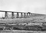Eine 52 mit Kondenstender vom Bw Nikolajew führt die Belastungsprobe auf der abenteuerlich anmutenden Pfeilerbrücke über den südlichen Bug durch. Neben dem 300 m langen wiederhergestellten Kastenbrückenteil über den Fluss (vgl. Bild-Nrn. 18852 - 18856) führten die restlichen 700 m über diese Gerüstpfeilerbrücke an der Strecke Nikolajew (Mykolajiw) - Kolosowka. Auf ihrem Rückzug 1941 zerstörte die Rote Armee die stattliche Zahl von 3544 Brücken, die den Eisenbahnbetrieb nachhaltig störten. Bis Mai 1943 ließen sich trotz schwieriger Materialbeschaffung 2076 Brücken mit einer Gesamtlänge von rund 55 km zumindest provisorisch wiederherstellen. Danach finden die Deutschen an, die gerade wiederhergestellten Brücken vor an vorrückenden Roten Armee wieder zu sprengen. Die imposante Brücke über den südlichen Bug besteht auch heute noch aus der 700 m langen Pfeilerkonstruktion (Stelzen) und der sich anschließenden Strombrücke aus drei 100 m langen Parabel-Fachwerkträgern. (1943) <i>Foto: Walter Hollnagel</i>
