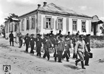 Blaue Eisenbahner, die alle verschiedene Schießprügel tragen und von einem Polizisten geführt werden, auf dem Weg zum Schießplatz in Snamenka. (1943) <i>Foto: Walter Hollnagel</i>
