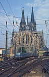 Vor dem Kölner Dom, der weltweit zu den größten Kathedralen im gotischen Baustil zählt, fährt 110 117 mit einem Eilzug aus dem Hauptbahnhof. (03.08.1980) <i>Foto: Joachim Bügel</i>