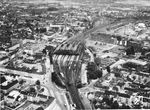 Luftbildaufnahme auf die Anlagen von Mönchengladbach Hbf mit der dominierenden Bahnhofshalle, gesehen von Süden aus. Die Gleise von unten erreichen den Hauptbahnhof aus Richtung Rheydt. Oben verzeigen sich die Gleise nach Neuss (rechts) und Viersen. Im Gleisdreieck liegt das Bahnbetriebswerk. (1960) <i>Foto: BD Wuppertal</i>