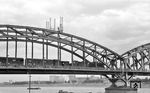 Eine 50er mit Kabinentender überquert den Rhein über die Kölner Südbrücke auf dem Weg zu den rechtsrheinischen Rangierbahnhöfen Gremberg oder Kalk-Nord. Offenkundig finden gerade Restaurationsarbeiten auf den Brückenbögen statt. (1959) <i>Foto: Fischer</i>