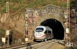 ICE 628 (München - Essen) verlässt den 930 m langen Schwarzkopftunnel bei Heigenbrücken. Nach Fertigstellung der neuen Spessartrampe soll der Schwarzkopftunnel verfüllt werden. Vermeintlich machte der Tunnel seit seiner Inbetriebnahme immer wieder Probleme. Der einzige senkrechte Abluftschacht reichte angeblich bis zur Elektrifizierung der Strecke nicht aus, um die Abgase der Dampflokomotiven dauerhaft aus dem Tunnel abziehen zu lassen. Bei der Elektrifizierung 1957 wurde die Tunnelsohle um 60 Zentimeter tiefer gelegt, was die Statik der Gleislage negativ beeinflusste. Um 1926 und 1970 wurde der Tunnel saniert, da der Gebirgsdruck und eindringendes Bergwasser die Gewölbemauerung beschädigt hatten. Auch 1991 soll es zu einem Wassereinbruch in den Tunnel gekommen sein, woraufhin 1993 für sechs Millionen DM eine Betonschale eingebaut wurde. Nachdem sich 2010 ein Teil dieser Schale wieder gelöst habe, wurden 300 Deckenanker gesetzt und der Tunnel mit einem elektronischen Meßsystem überwacht. Trotzdem gab es weiterhin Probleme, u.a. mit Eiszapfenbildungen im Winter. Mit einer Geschwindigkeit von 70 km/h zählt der Schwarzkopftunnel heute zu den am langsamsten befahrenen Tunneln im Fernverkehrsnetz der Deutschen Bahn. (03.12.2016) <i>Foto: Joachim Bügel</i>