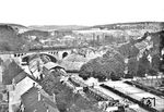 Blick von der Evangelischen Kirche in Wuppertal-Sonnborn auf eine P 8, die gerade über die Wupperbrücke am Zoo westwärts fährt. Unten die Schwebebahnstation "Am Zoo", mit einem damals noch hölzernen Übergang über die Wupper. Rechts die Tennisanlagen des (nicht mehr sichtbaren) Stadions, oben rechts die Anlagen der Bayer-Werke und der Blick auf den fast noch unbebauten Nützenberg. (1928) <i>Foto: RBD Wuppertal</i>