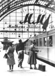 Feucht-fröhliche Abschiedsszene am F 21 (Rheinpfeil) mit einer Flasche Schaumwein aus einer Eltviller Sektkellerei, die in großen Buchstaben an der Bahnhofshalle beworben wird. (1953) <i>Foto: Willi Klar</i>