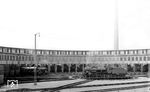 Aufgeräumt und kaum russgeschwärzt zeigt sich hier das Areal des Bw Düsseldorf Abstellbahnhof. Zum Aufnahmezeitpunkt war der 30-ständige Ringlokschuppen aus Stahlbeton erst ein Jahr alt. Das neue Bw diente als Ersatz des beengten Werkes am Hauptbahnhof und wurde nach neuesten Bau- und Betriebserkenntnissen erstellt (wie parallel das Werk in Derendorf). Das zum Maschinenamt Düsseldorf der Reichsbahndirektion Wuppertal gehörende Bw beschäftigte in den 1930er Jahren rund 600 Mitarbeiter. Auf der Drehscheibe befindet sich die hier stationierte 38 3248. Links im Schatten sind eine 78er und 91.3 zu erkennen. Im Zweiten Weltkrieg wurde das Bw schwer beschädigt, aber weiterhin komplett genutzt. Nach Ende der Dampflokzeit Mitte der 1970er Jahre wurde das Bw für die Wartung der S-Bahnen zuständig. Diese Aufgabe hat das Werk bis heute inne. Der Ringlokschuppen blieb seit den 1970er Jahren ungenutzt. 1991 nahm die Landeshauptstadt Düsseldorf ihn in die Denkmalliste auf. Das verhinderte jedoch nicht den weiteren Verfall. Die Suche nach einer neuen Nutzung blieb erfolglos, obwohl Pläne sehr weit gediehen waren, im Ringlokschuppen historische Schienenfahrzeuge unterzubringen. Schließlich übernahm den Ringlokschuppen eine privat-museale Institution für historische Autos, um dort eine Dependance zu eröffnen. Der Umbau und Restaurierung des Schuppens kostete 15 Millionen Euro, seit 16. September 2006 beheimatet er die Oldtimer der Classic Remise Düsseldorf. (20.05.1932) <i>Foto: DLA Darmstadt (Bellingrodt)</i>