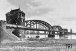 Blick auf die am 30.11.1900 eingeweihte 961 m lange zweigleisige, eiserne Bogen-Fachwerkträgerbrücke über den Rhein bei Worms an der Bahnstrecke nach Darmstadt. Diese Konstruktionsart wurde in Deutschland erstmals bei einer Eisenbahnbrücke angewendet und kam später, wie bei der Kölner Südbrücke, noch öfter zur Ausführung. Die Strombrücke wurde durch zwei massive Tortürme eingerahmt. Am Ende des Zweiten Weltkriegs wurde die Rheinbrücke am 20. März 1945 durch deutsche Truppen gesprengt. 1948 wurde eine Behelfsbrücke errichtet, die erst 1960 durch ein endgültiges Bauwerk ersetzt wurde. Die Gleise im Vordergrund sind Anschlussgleise zum Hafen. (1934) <i>Foto: RVM</i>