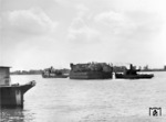Ein Schlepper hat mit einem voll beladenen Ponton-Floß den Fährhafen Cherson erreicht. Mittels Begleitschiff wird die Fuhre aus der Fahrrinne an die Anlegestelle bugsiert. Der provisorische Eisenbahnfährverkehr wurde im Sommer 1942 aufgenommen, nachdem die Bahnanlagen nebst Anlegestellen in Cherson Fähre und Aljeschki Fähre fertiggestellt waren. (1943) <i>Foto: Walter Hollnagel</i>