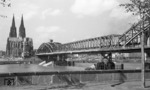 Blick vom Deutzer Ufer auf die provisorisch mit einem SKR-Stahlüberbau wiederhergestellte Hohenzollernbrücke mit dem Kölner Dom. Auf der Brücke ist eine pr. G 8 (Baureihe 56.2) mit einem Personenzug auszumachen. (1949) <i>Foto: Fischer</i>
