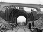 Der Königsdorfer Tunnel war ein 1623 m langer Eisenbahntunnel auf der Strecke Köln - Aachen bei Horrem. Der Tunnel blieb bis 1954 in Betrieb und wurde dann innerhalb eines Jahres komplett abgetragen. Zuvor hatten aggressives Bergwasser und Abgase der Dampflokomotiven das Mauerwerk des Tunnels geschädigt sowie Ausspitzungen am Gewölbemauerwerk in den Jahren 1937/38 die Standsicherheit stark reduziert. Daher kam nur noch eine Beseitigung des Bauwerks in Betracht. Während der Rückbauarbeiten fuhren weiterhin in den Abtragungspausen Züge durch den verbleibenden Rest-Tunnel. Das Bild zeigt die Reste des ehemaligen Tunnelportals auf der Königsdorfer Seite während eines Pressebesichtigungstermins.  (12.05.1955) <i>Foto: Fischer</i>
