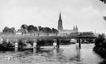Der Ulmer Klassiker mit Münster und Donaubrücke ist heute nicht mehr möglich, da die Brücke komplett mit Lärmschutzwänden eingehaust wurde. Anfang der 1950er Jahre überquert vermeintlich 50 389 die Donau. Am 24. April 1945, wenige Tage vor dem Ende des Zweiten Weltkriegs und kurz vor dem Einmarsch der US-Truppen, wurde die Eisenbahnbrücke ebenso wie alle anderen Ulmer Donaubrücken gesprengt. Im Mai wurde eine hölzerne Behelfsbrücke eingerichtet. Erst im Oktober 1949 konnte die Brücke durch Stahlträger verstärkt werden. Zwischen 1955 und 1957 wurde die Brücke zwischen Ulm und Neu-Ulm neu gebaut. (07.1951) <i>Foto: Carl Bellingrodt</i>