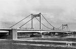 Bis 1927 war (Cöln-)Mülheim durch eine Schwimmbrücke mit dem linksrheinischen Ufer verbunden. Die Stadt Cöln hatte sich mit dem Eingemeindungsvertrag von Mülheim am 1. April 1914 zum Bau einer festen Brücke verpflichtet. Aufgrund des Ersten Weltkriegs und der Inflationszeit wurden erste Schritte zur Realisierung jedoch erst in den 1920er Jahren eingeleitet, Baubeginn war am 19. Mai 1927. Oberbürgermeister Konrad Adenauer eröffnete am 13. Oktober 1929 die neue Hängebrücke (Foto), die auch von der Straßenbahn benutzt wurde. Das Bauwerk wurde als sog. "unechte Hängebrücke" ausgeführt. Dabei wurden die Zugkräfte der Tragseile vom versteiften Fahrbahnträger als Druckkräfte aufgenommen. Somit konnten schwere Ankerblöcke vermieden werden, die damals im Kölner Baugrund als nicht ausführbar betrachtet wurden. Im Zweiten Weltkrieg wurde die Brücke durch einen Luftangriff am 14. Oktober 1944 zerstört. Mit dem Neubau wurde 1948 begonnen. Interessanterweise erfolgte die Einweihung der neuen Brücke am 8. September 1951 wieder in Anwesenheit Adenauers, diesmal als Kanzler der Bundesrepublik Deutschland. (1933) <i>Foto: Carl Bellingrodt</i>