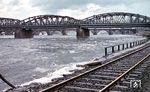 Frühjahrshochwasser an der Mosel in Koblenz. Vorne die (alte) Eisenbahnbrücke, die Lützel und den Hauptbahnhof verbindet, dahinter die Balduinbrücke. Das Gleis im Vordergrund bildete die Verbindung zwischen Moselweiß und dem Moselhafen, der sich zwischen Balduinbrücke und dem Deutschem Eck erstreckte und 1969 endgültig aufgegeben wurde. An deren Stelle trat der neue Rheinhafen (Rheinkilometer 596,5), der am 25. Januar 1965 offiziell seiner Bestimmung übergeben worden war. Das Gleis war damit entbehrlich geworden und wurde zurückgebaut. (03.1956) <i>Foto: Carl Bellingrodt</i>